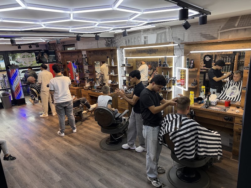 De barbershop aan de Markt in Ommen op een drukke dag: vijf kappers aan het werk, gestreepte kapmantels en verlichte spiegels.